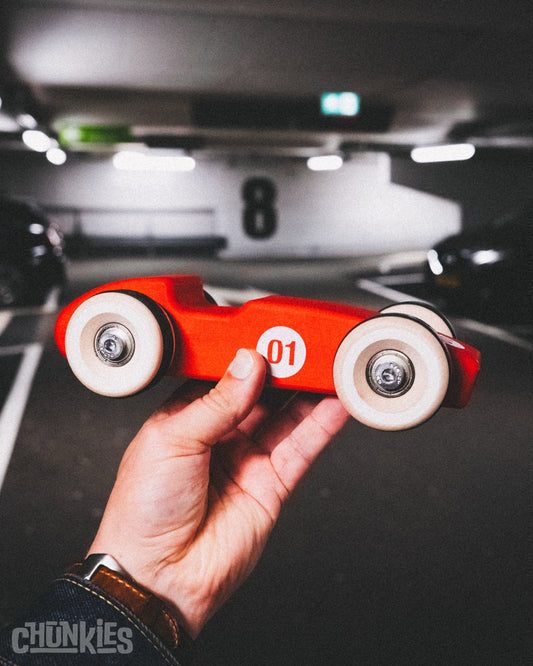 Hand holding solid wooden toy car Chunkies No. 01 to show large scale and heavyweight quality. With a length of 22 centimeters and a weight of about 600 grams you can feel it's quality. All solid European maple wood. Made in Germany. Hand finished and assembled in The Netherlands. Sustainable and fun and open ended play.