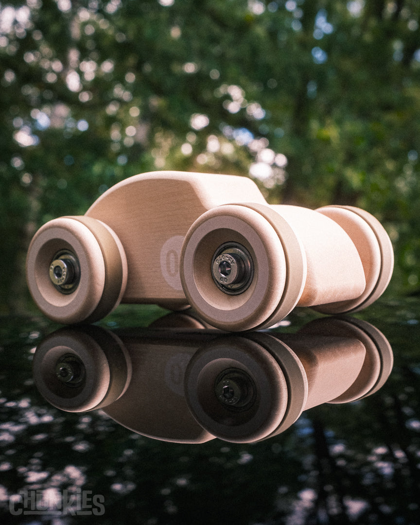 Chunkies The Bug wooden toy car in natural European maple wood on a reflective surface with a forest in the background