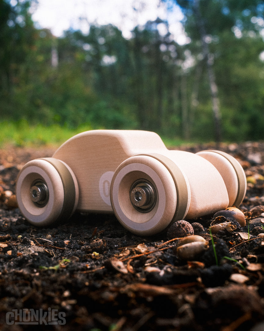 A 3/4 view of maybe cutest Chunkies wooden toy car shaped like a vintage Beetle in a forest environment. Solid European maple wood. Made in Germany. Child and planet safe.